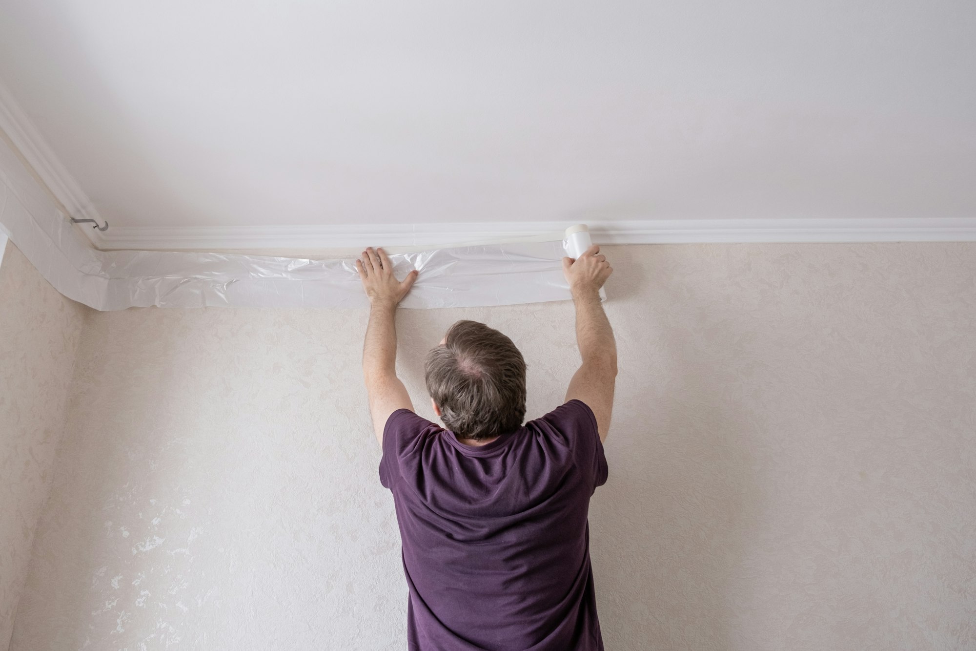 Middle aged man glues cover film with masking tape to protect the walls. Apartment renovation.