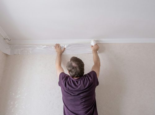 Middle aged man glues cover film with masking tape to protect the walls. Apartment renovation.